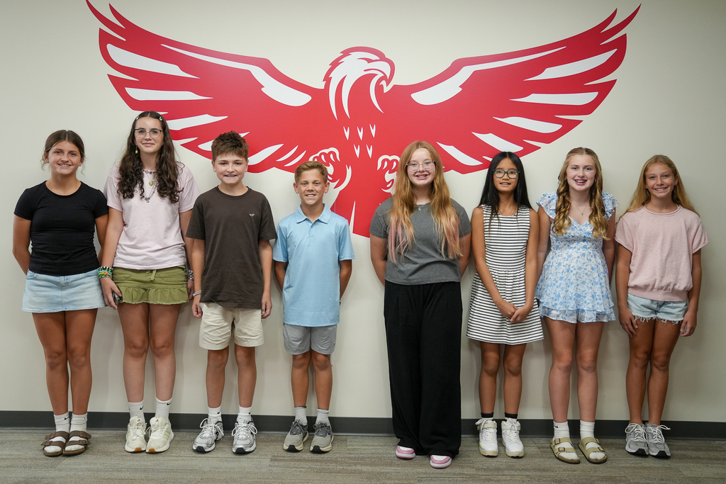Eight Milford Middle School featured student artists pose together in front of a large red Milford Eagle mural.