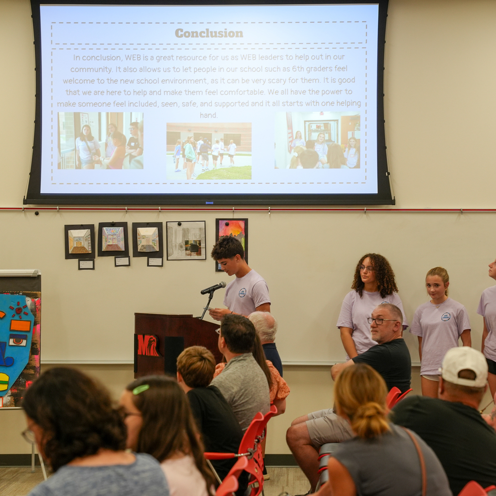 A Milford Middle School WEB leader speaks at the podium while fellow WEB leaders stand nearby during their presentation to the Board of Education.