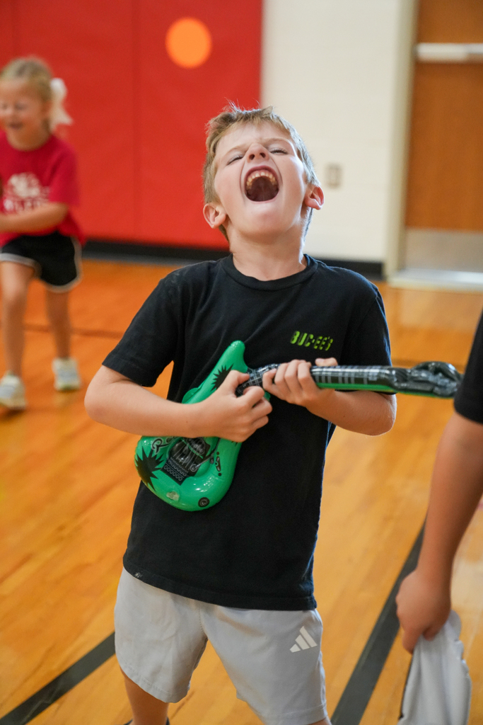 A Seipelt student pretends to perform with a green inflatable guitar while dancing in the gym.