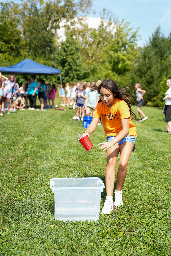 A Seipelt student races to pour water from a red cup into a container during an outdoor relay.