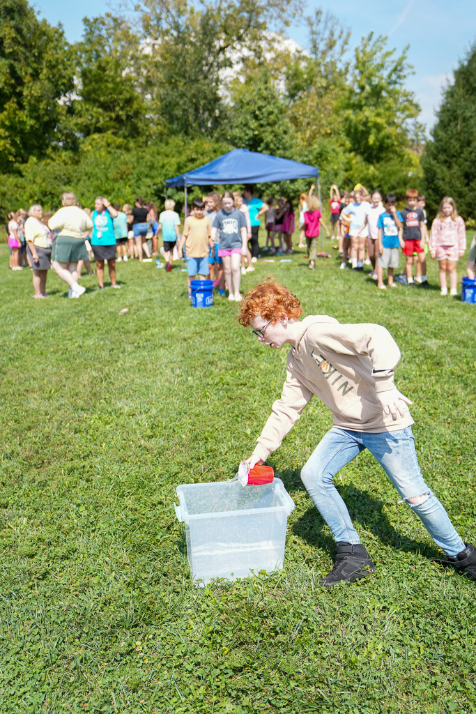 A Seipelt student pours water from a red cup into a container during the outdoor walk-a-thon activities.