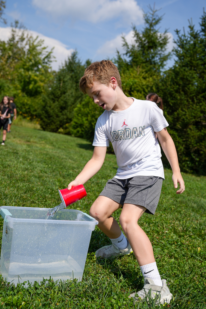 A Seipelt student pours water from a red cup into a container during the Drip, Dash and Dance triathlon.