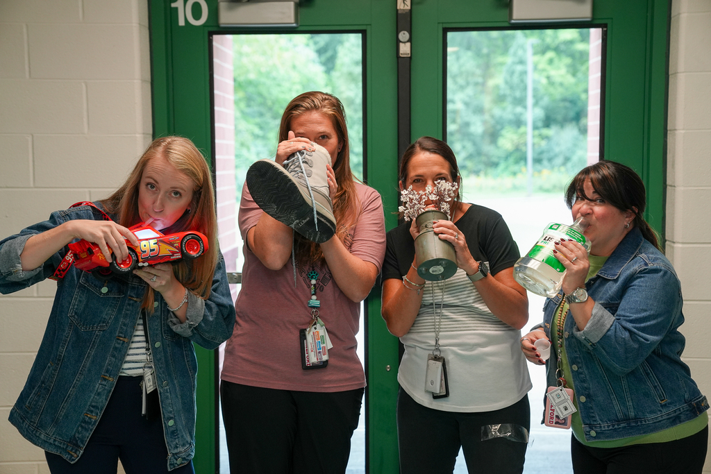 Four staff members pose with creative drink containers, including a toy car, boot, flowerpot and large plastic jug.