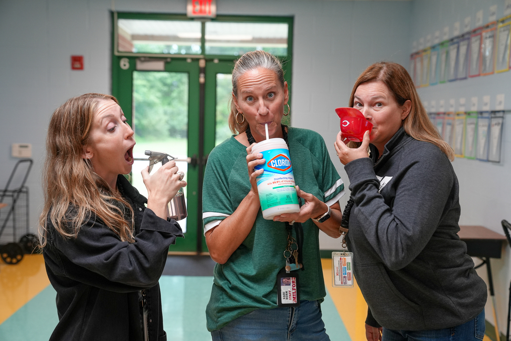 Three staff members pose with unusual containers, including a spray bottle, disinfecting-wipes container and small red funnel.