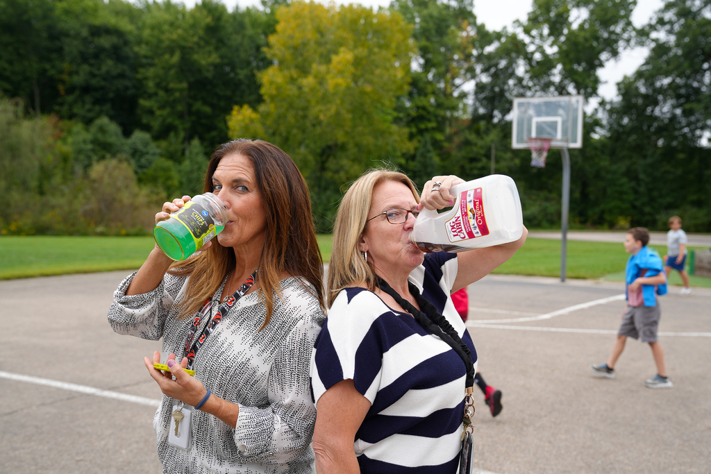 Two staff members participate in “Anything but a Water Bottle Day,” drinking from a pickle jar and a plastic tea jug outside the school.
