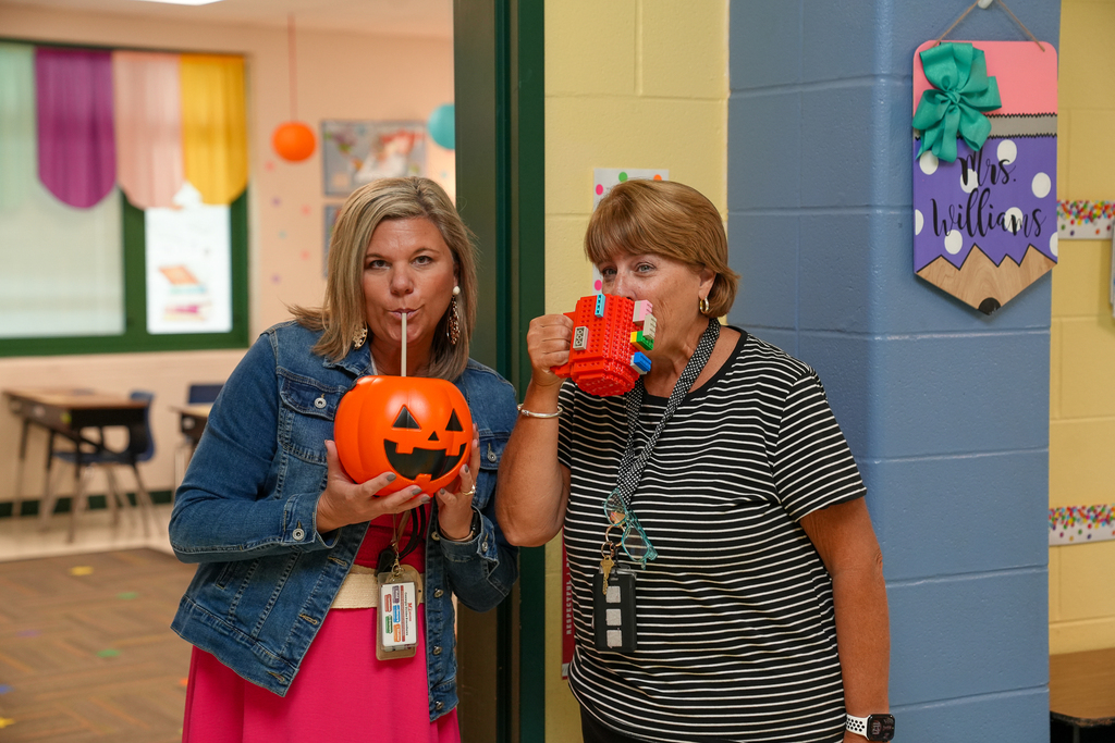Two staff members drink from a plastic jack-o’-lantern and a colorful mug made from building blocks.