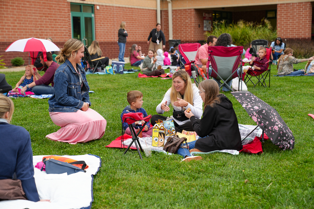 A staff member talks with several students seated on a blanket during Lunch on the Lawn.