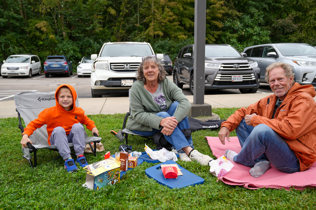 Students and adults enjoy lunch together on blankets and folding chairs outside the school.