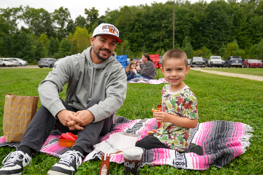 A student and an adult smile while eating lunch together on a picnic blanket.