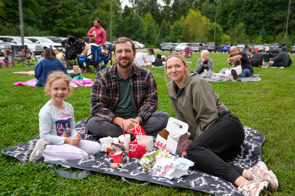 A student and two adults pose together with their lunches during the outdoor event.