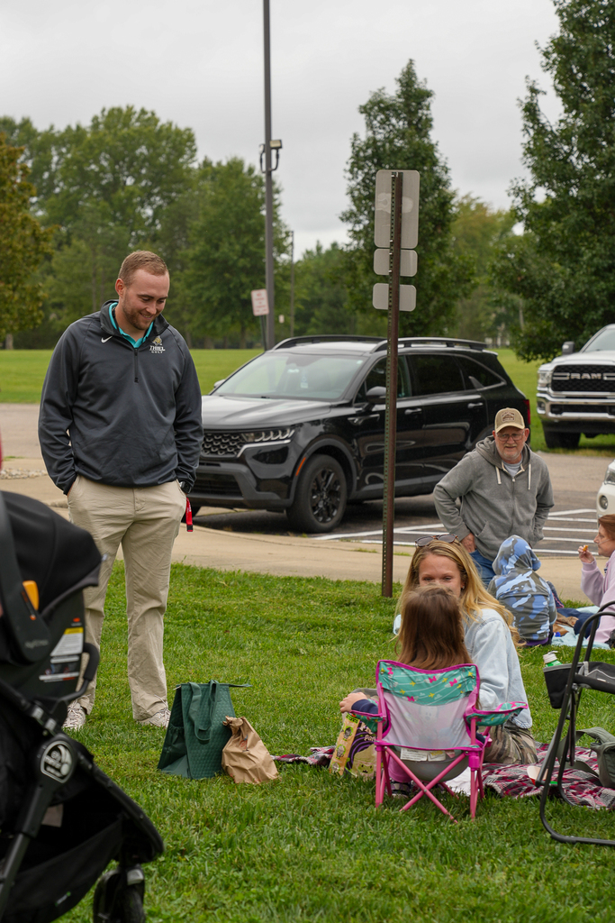 Students and adults enjoy lunch together on blankets and folding chairs outside the school.
