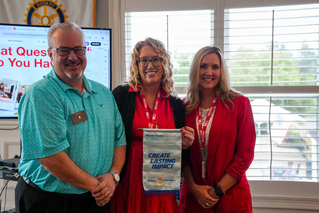 A Cincinnati-Eastside Rotary member stands with Milford Schools Superintendent Dr. Bobbie Fiori and Director of Teaching and Learning Misty Goetz. They hold a Rotary banner reading “Create Lasting Impact.”