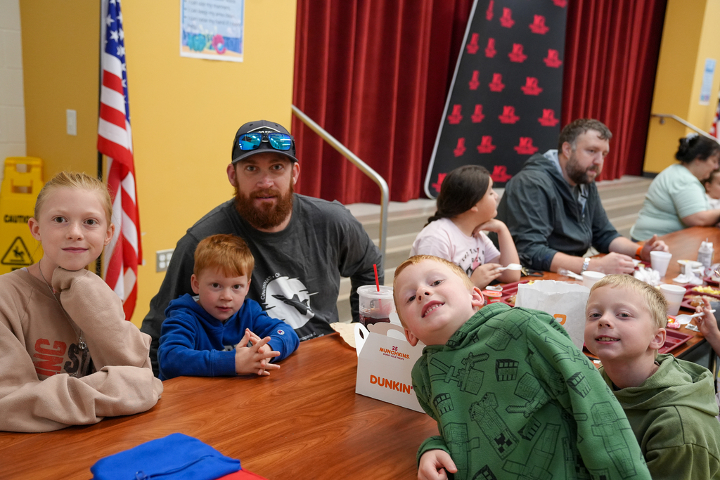 An adult and four children gather around a cafeteria table during breakfast.