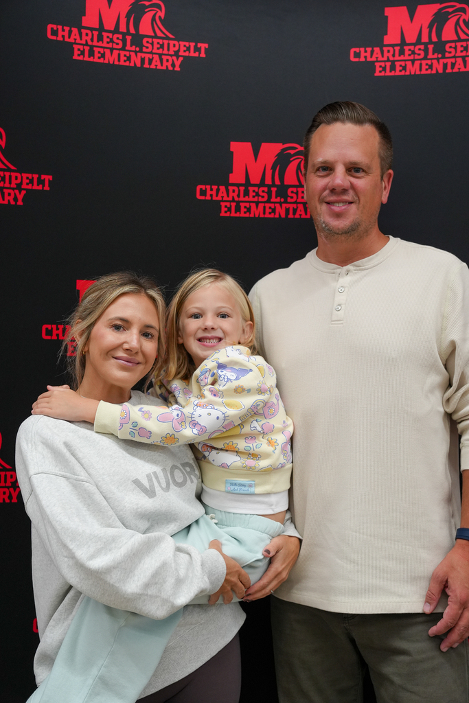 Two adults and a young child pose together in front of a Charles L. Seipelt Elementary backdrop.