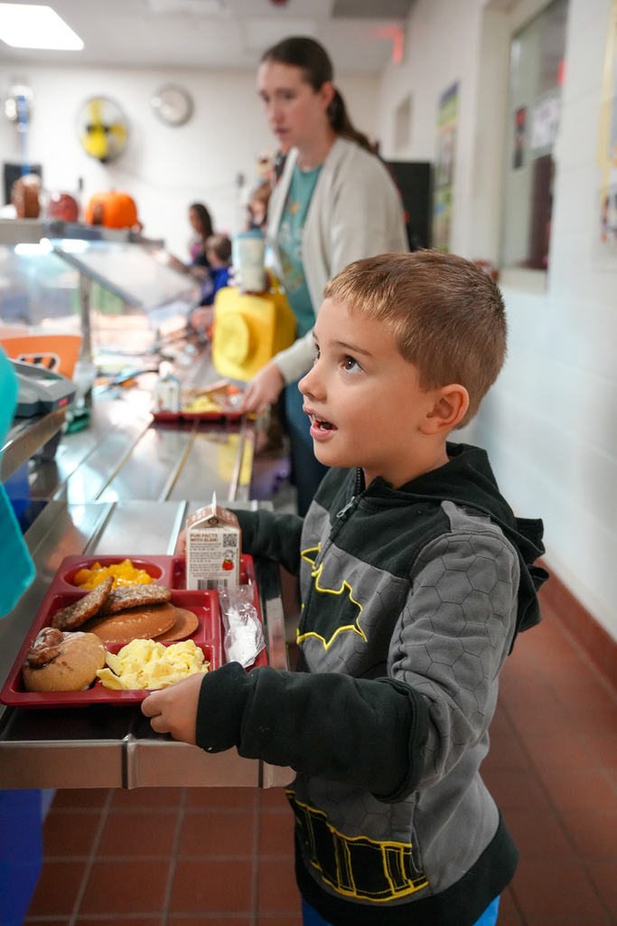 A student carries a breakfast tray through the cafeteria serving line.