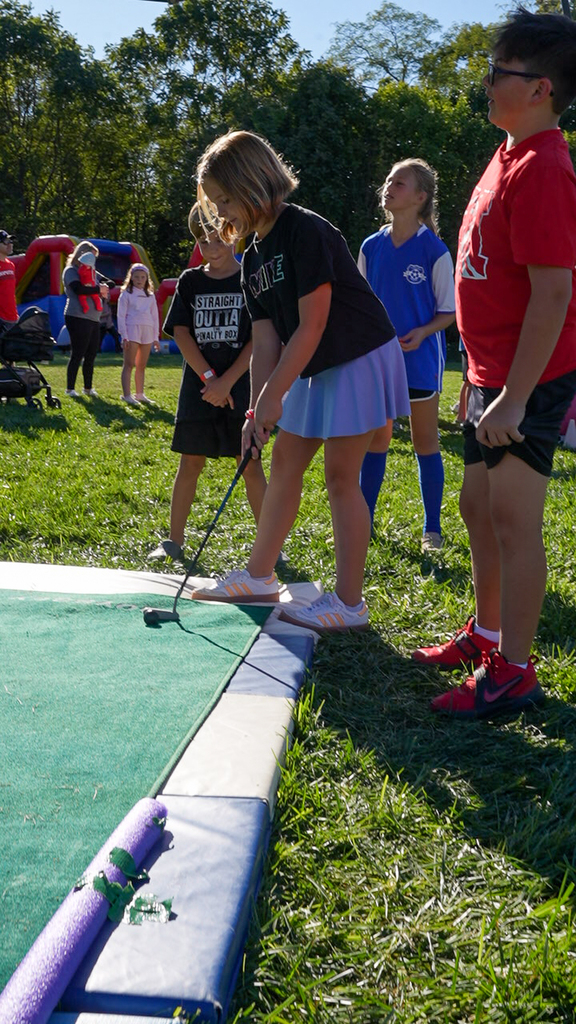 A McCormick Elementary student plays miniature golf outdoors during McCormick Fest as other students wait nearby.