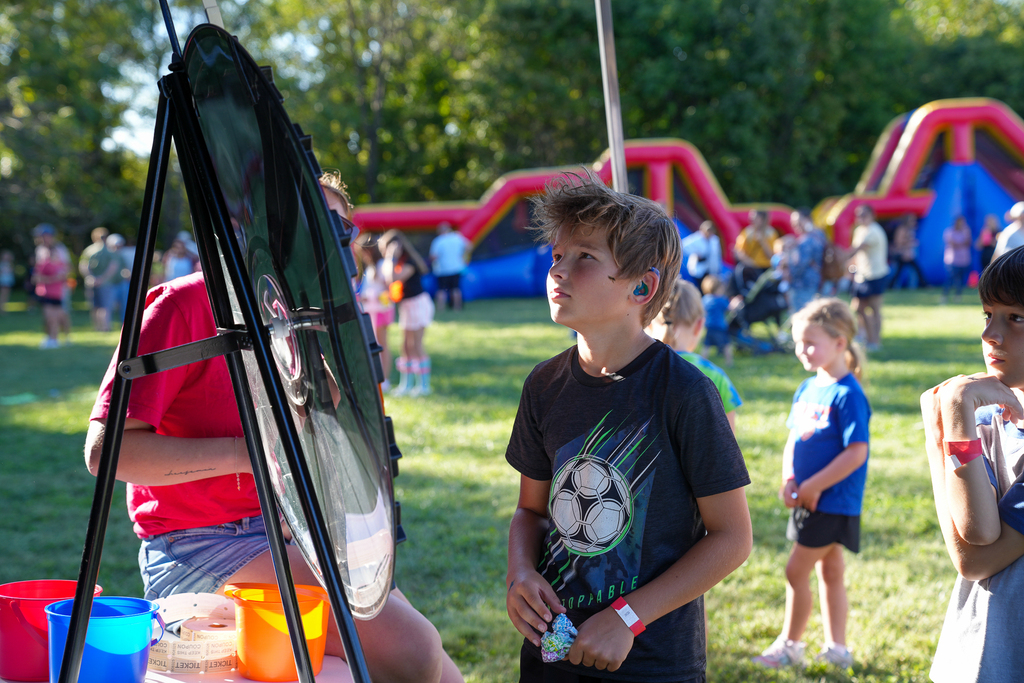 A student participates in a prize game at McCormick Fest, with inflatable activities and other families visible in the background.