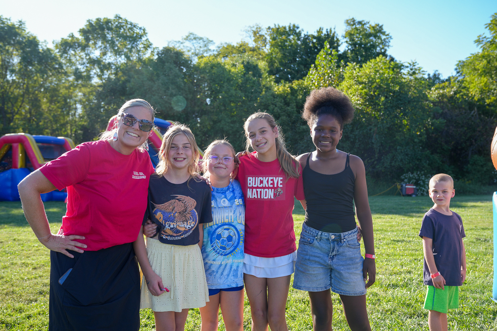 A McCormick staff member and four students smile together during McCormick Fest, with inflatable activities in the background.