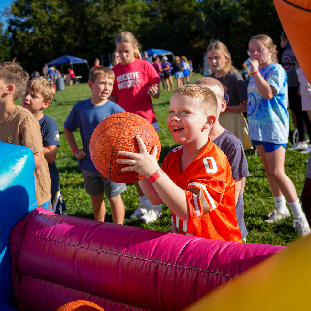 A smiling student holds a basketball while playing a game at McCormick Fest as other students wait their turn.