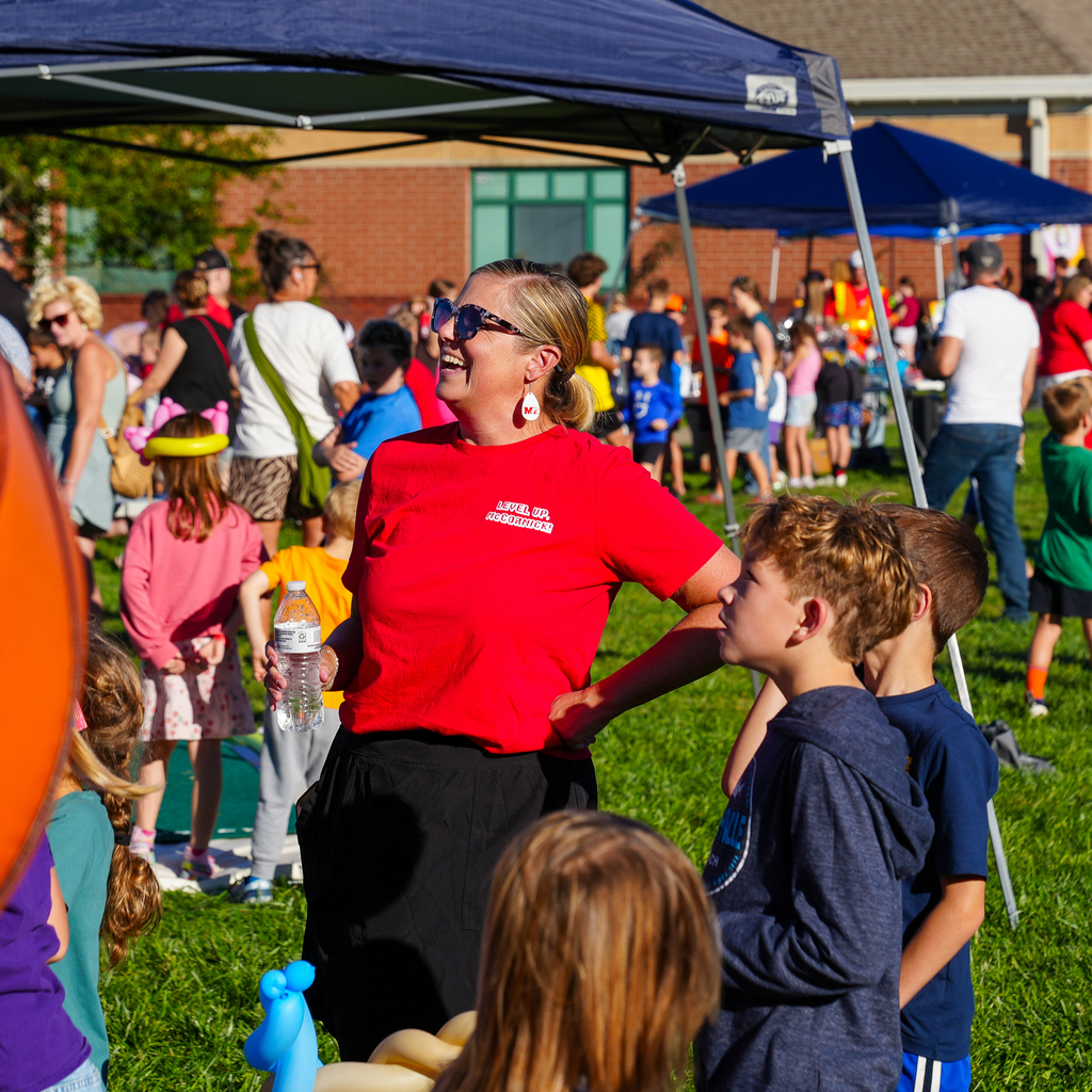 A McCormick staff member smiles while talking with students during McCormick Fest, with families and activities filling the school grounds in the background.