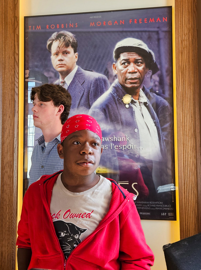 Two students stand in front of a Shawshank Redemption movie poster featuring Tim Robbins and Morgan Freeman.
