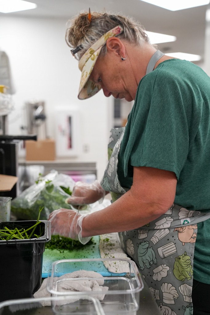 A Milford School Nutrition staff member wearing an apron and gloves prepares fresh greens in a school kitchen.