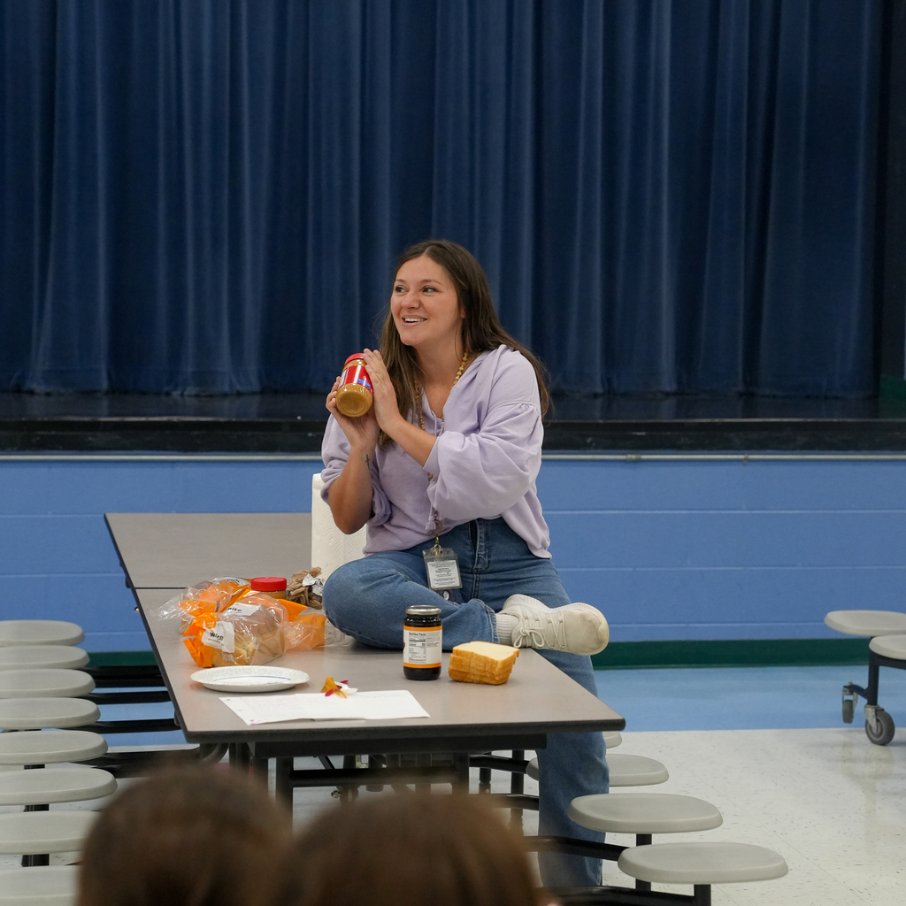 A McCormick Elementary staff member holds a jar of peanut butter while demonstrating how to follow written directions for making a peanut butter and jelly sandwich.