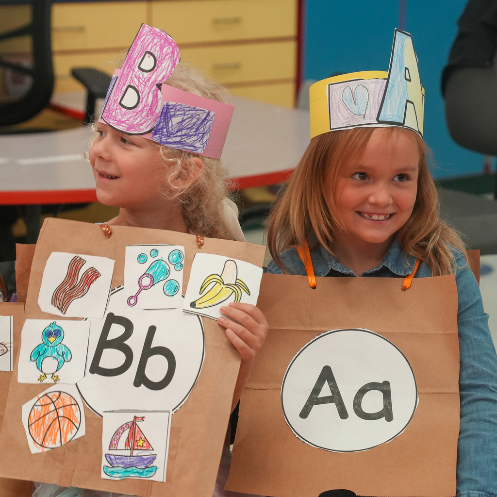 Two kindergarten students smile in handmade alphabet costumes featuring the letters B and A and pictures of objects beginning with their assigned letters.