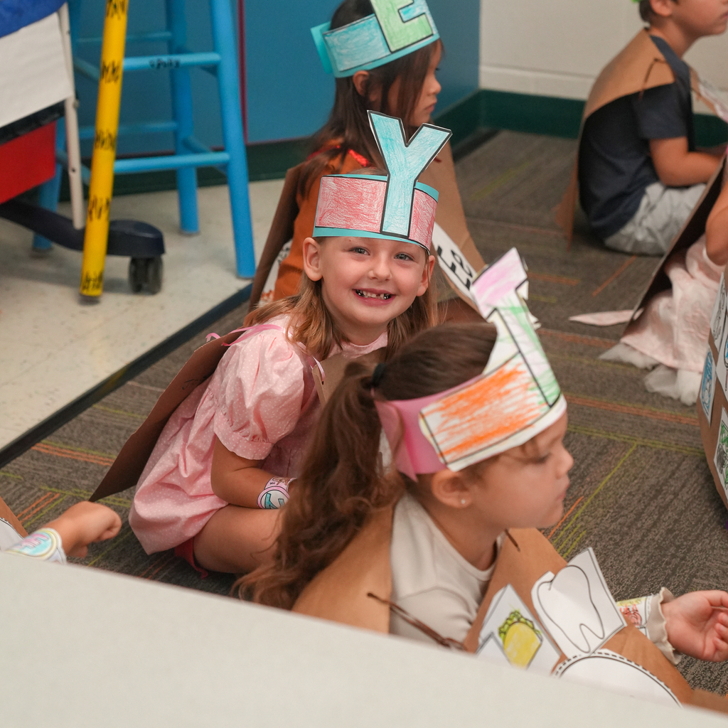 A kindergarten student smiles while wearing a handmade letter costume during an ABC fashion show.