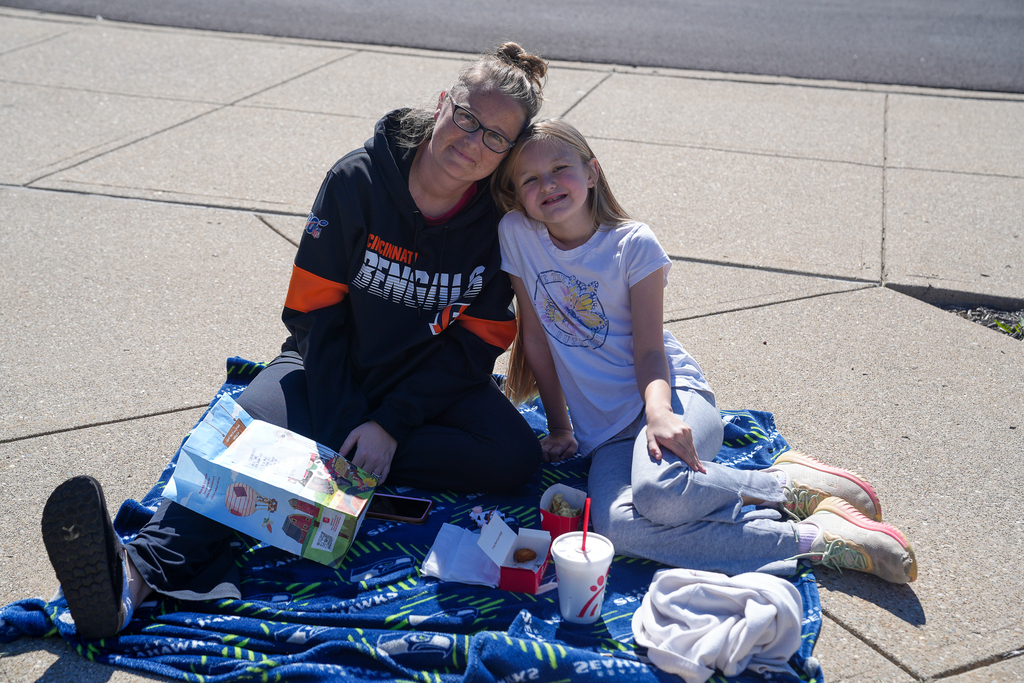 A student and an adult wearing a Cincinnati Bengals sweatshirt lean their heads together and smile while sitting on a blue blanket with lunch outside Mulberry Elementary.