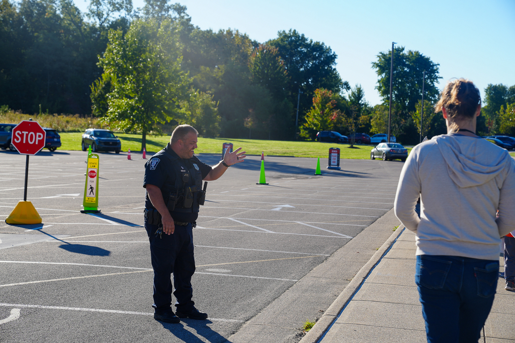 A uniformed police officer smiles and waves to people walking outside Mulberry Elementary on a sunny morning.