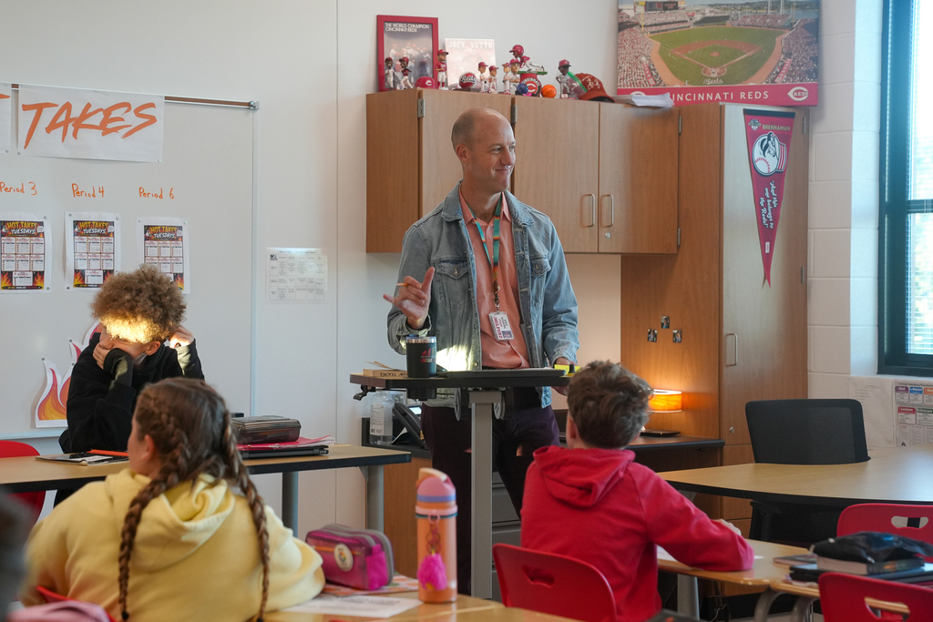 Mr. Huggins speaks to students seated at classroom tables during their weekly Hot Takes debate activity.