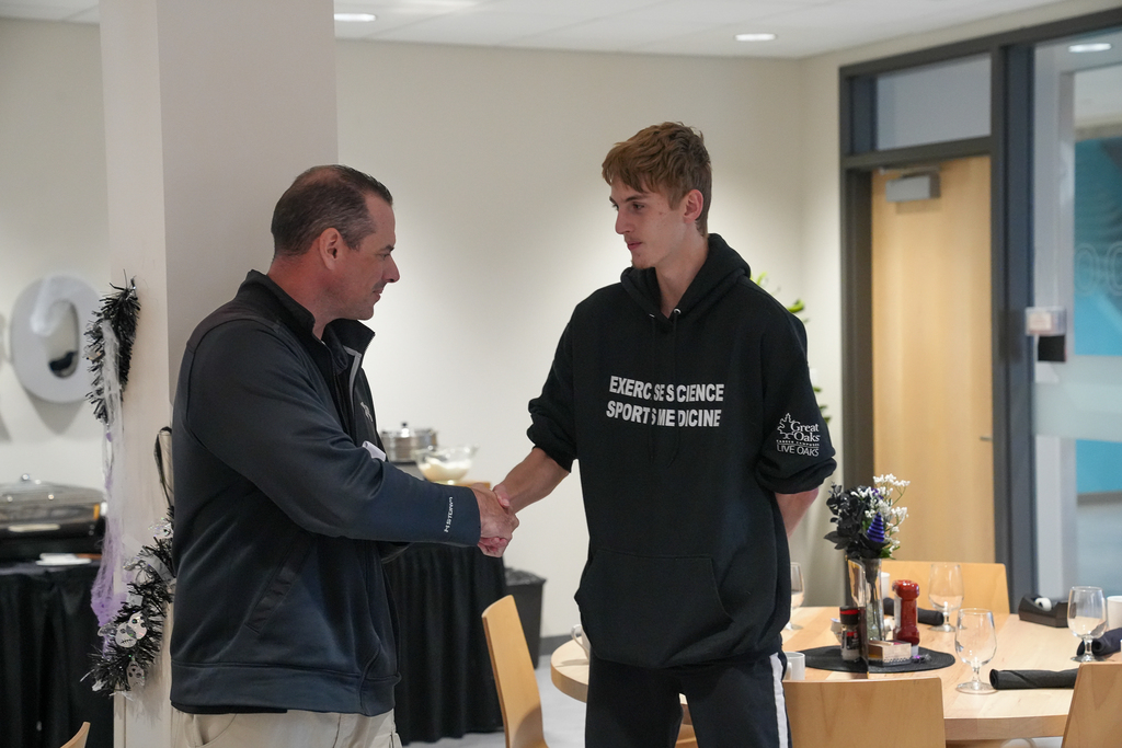 Milford student Andrew Dochterman shakes hands with a Great Oaks staff member during the Career Technical Excellence Awards recognition. Andrew is wearing a Live Oaks Exercise Science and Sports Medicine sweatshirt.