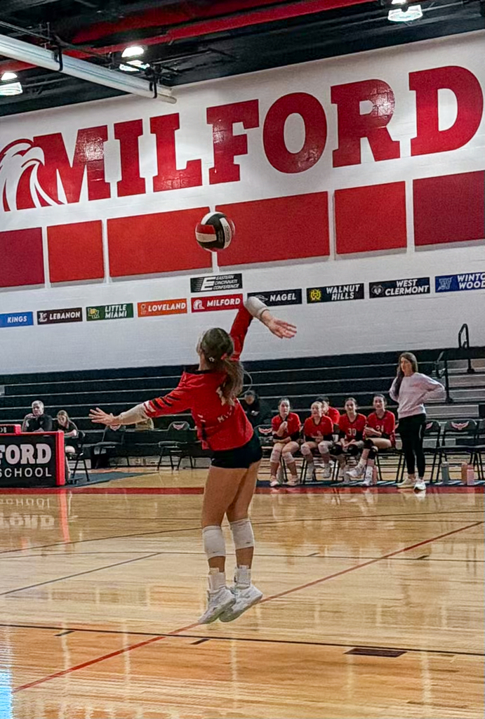 A middle school girl jumping for the volleyball