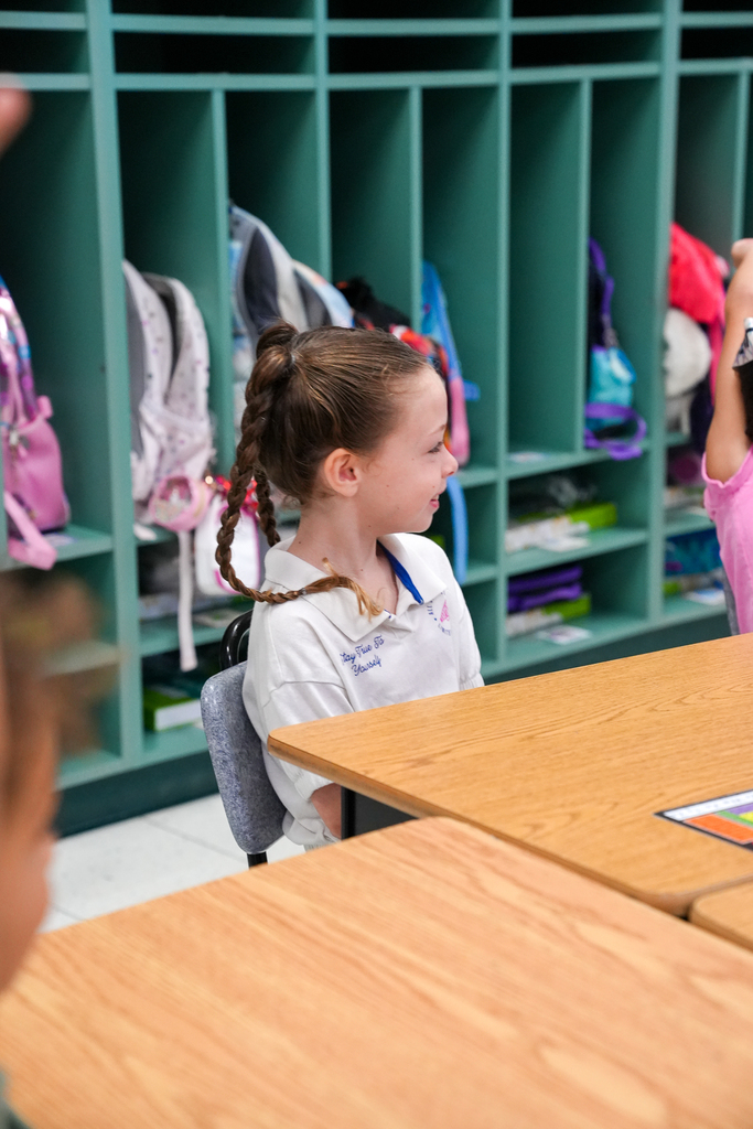 An elementary student smiles while sitting at her desk during a classroom visit from local firefighters.
