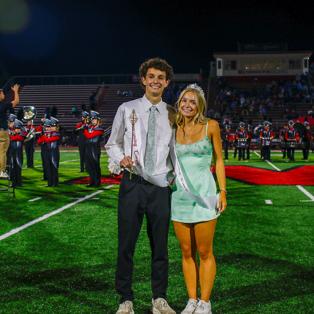 Two students pose together, one wearing a white shirt and tie and the other wearing a light green dress and tiara.