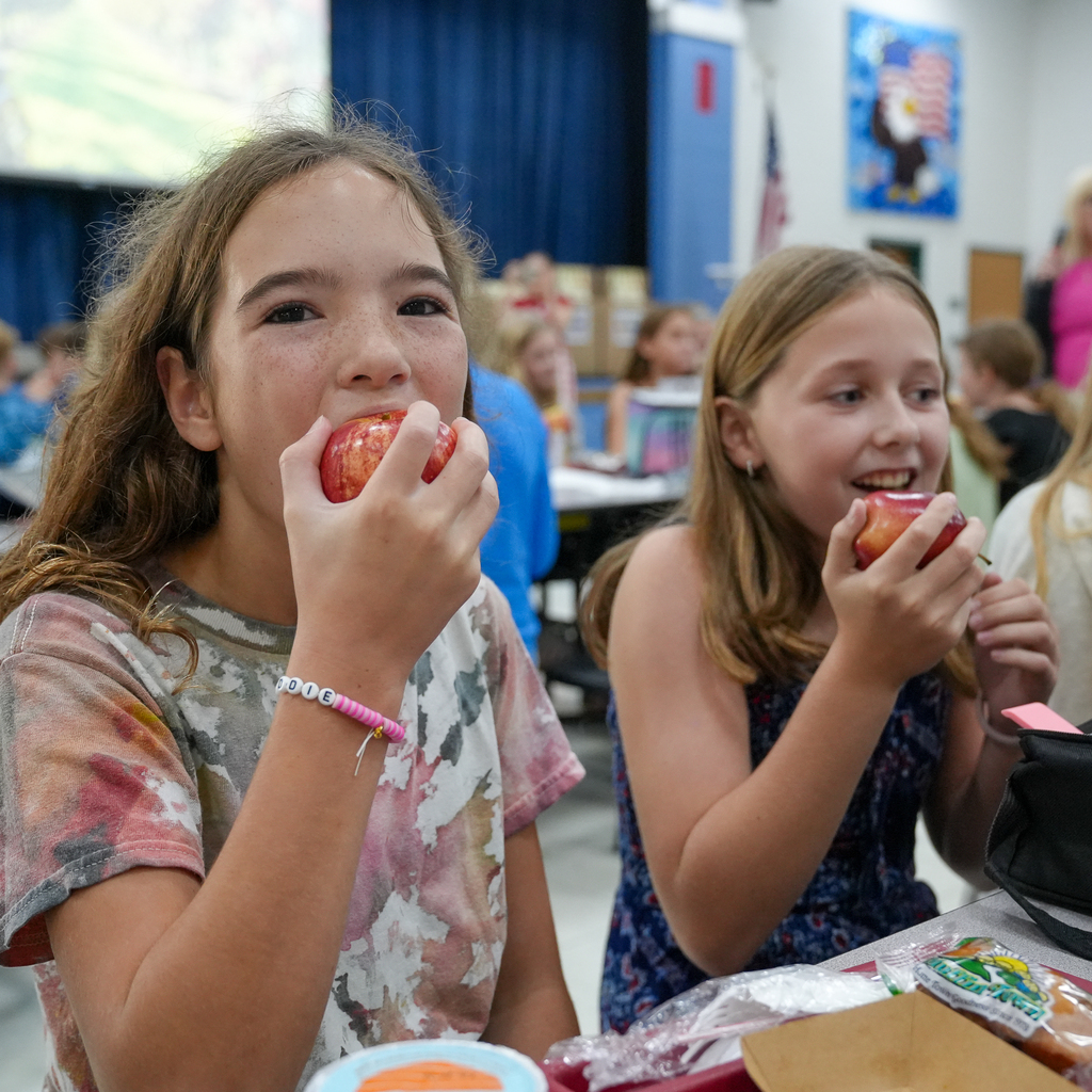 Two Pattison Elementary students smile at the camera while holding red apples during the Great Apple Crunch in the cafeteria.