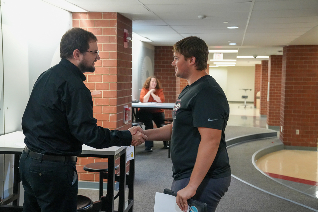 A student holding papers and a folder shakes hands with an adult interviewer during an FFA career preparation activity at Milford High School.