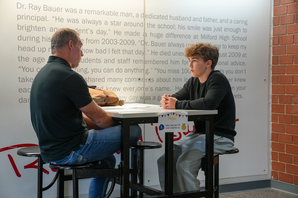 An adult interviewer gestures while speaking with a student in a black sweater at a table during the FFA Career Connections Lab.