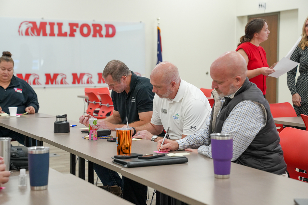 Business Advisory Council members write on sticky notes during a feedback activity while two facilitators stand nearby holding papers.
