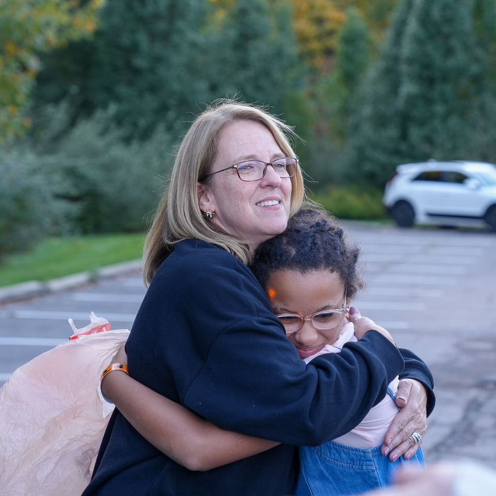 An adult and child share a hug outdoors at the fall festival.