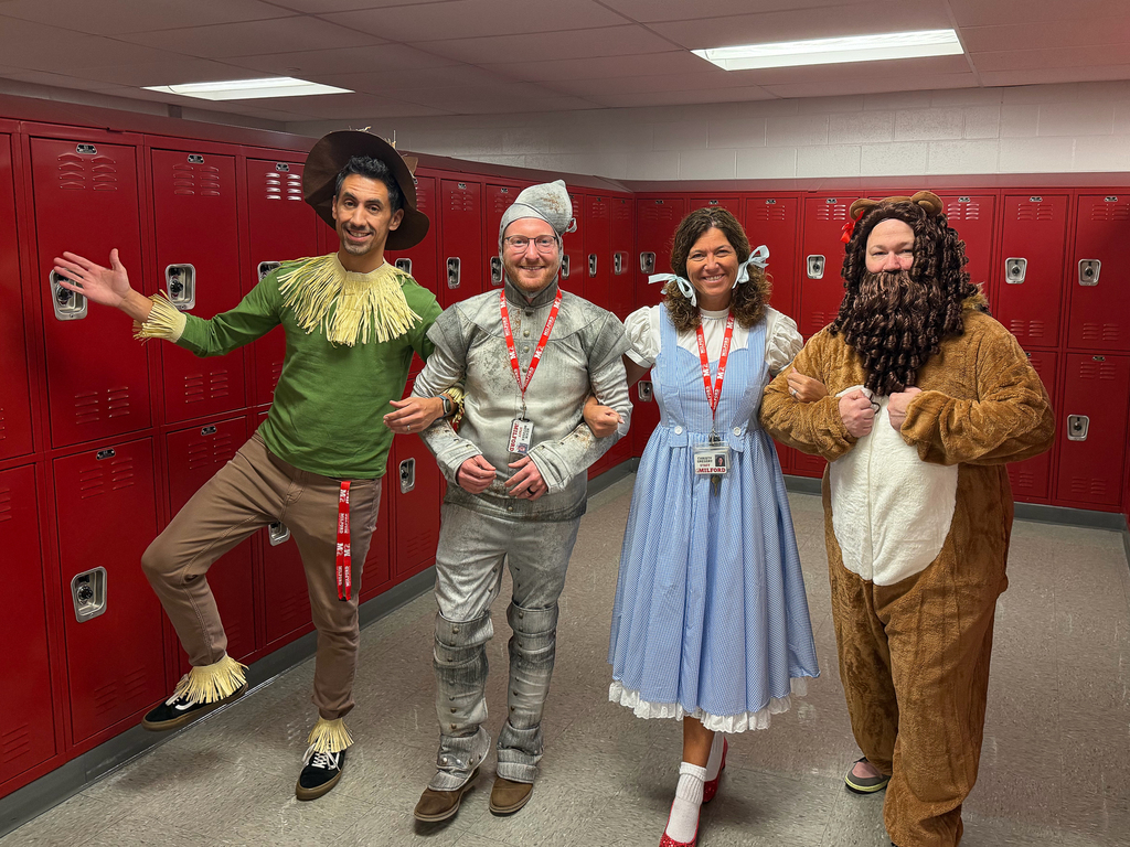 Four staff members pose in front of red school lockers dressed as the Scarecrow, Tin Man, Dorothy and Cowardly Lion from “The Wizard of Oz.”