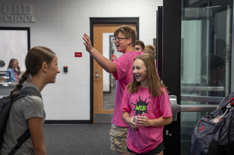 Boy and girl in pink "web" shirts holding the door