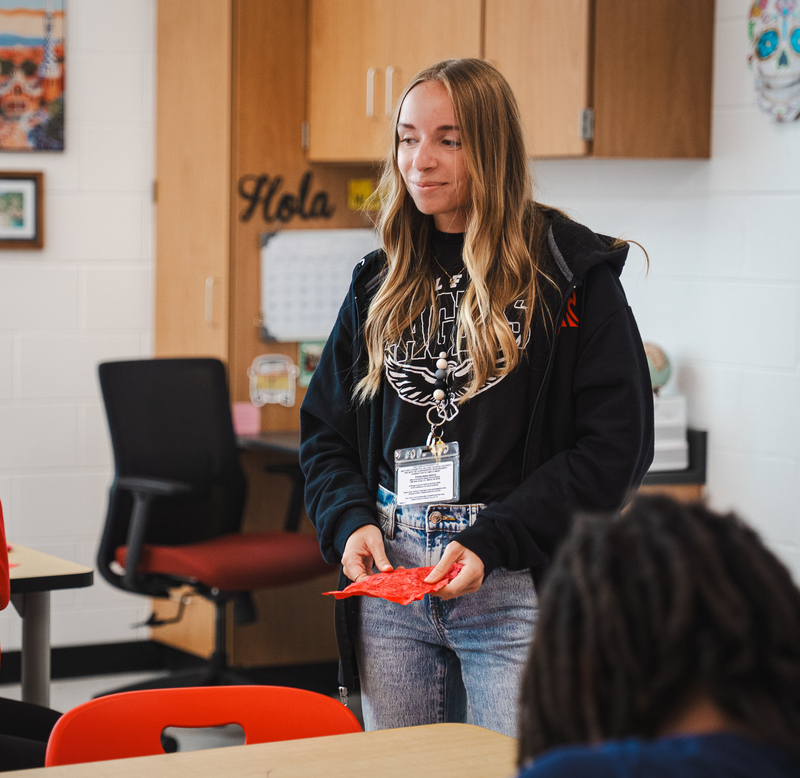 Young female teacher with blonde hair smiling in the distance wearing a black hoodie over a black Miflord shirt