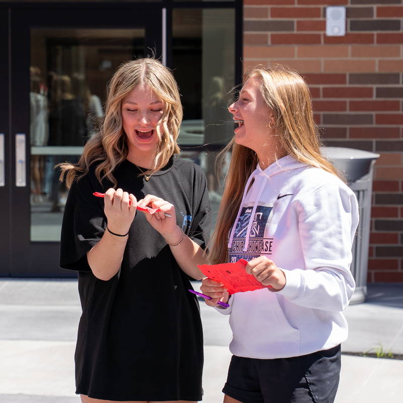 Two blonde female students laughing at their red piece of paper