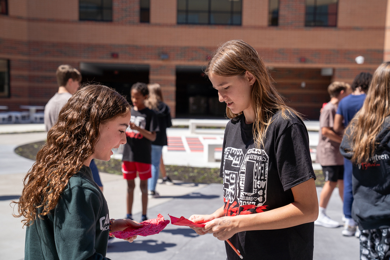 Two students talking to each other holding red pieces of paper