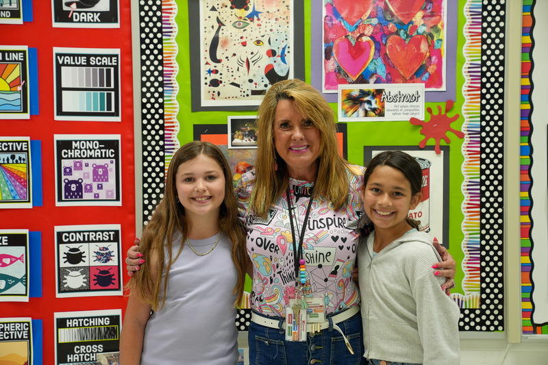 Students standing in front of artwork with their art teacher