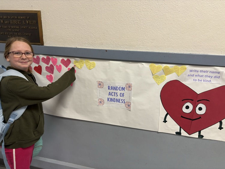 A photo of a student pointing to a cut out heart that showcases her random act of kindness.