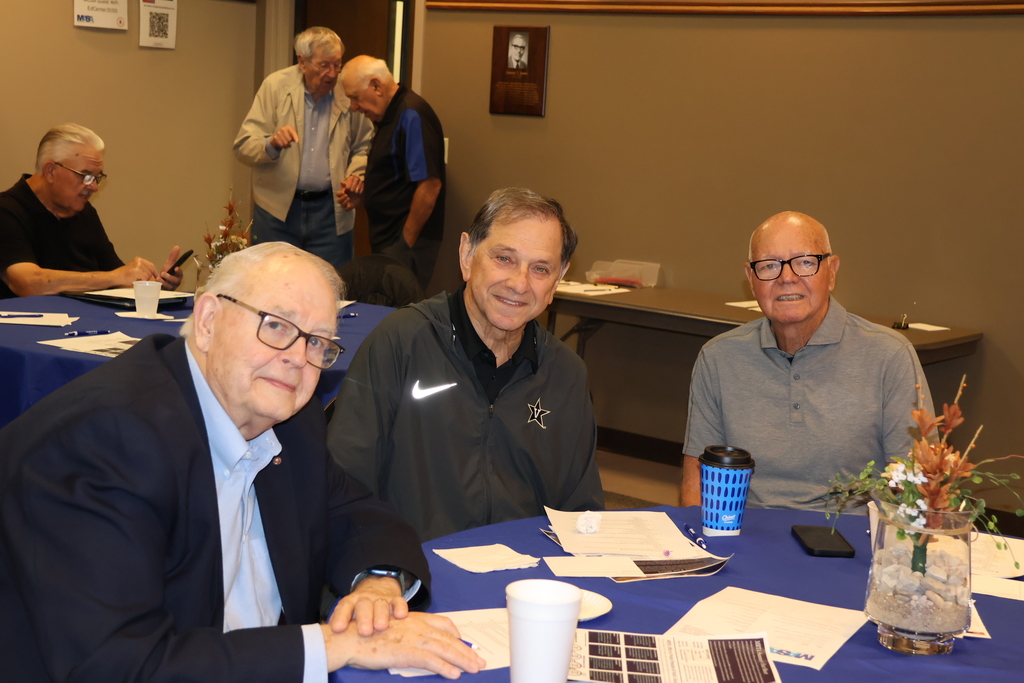 Three men sitting at a table pose for a picture.