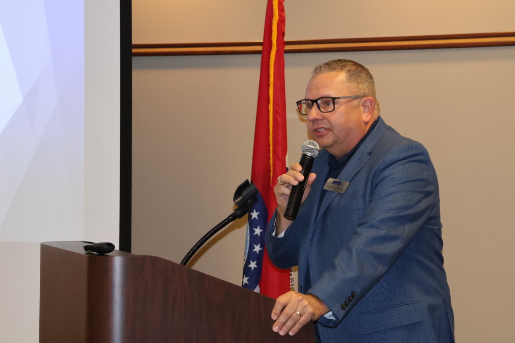 Dr. Mark Penny standing at the podium welcoming everyone.